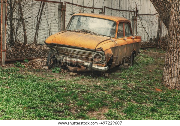 Wrecked orange old car. Junkyard. Old abandoned\
soviet vintage car.\
