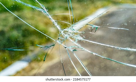 Wrecks on transparent glass against road and lawn closeup. Destroyed window on street. Affect of thrown item to show-window. Vandalism actions