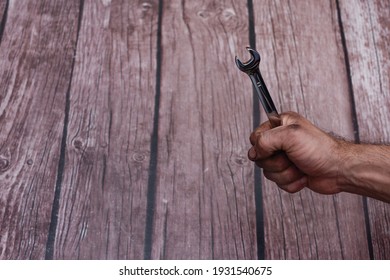 Wrench In Hand. The Oily, Dirty Working Hands Are Clenched Into A Fist With A Spanner. On A Wooden Background. Copy Space