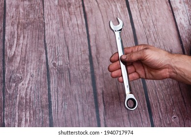a wrench with ratchet in a man's hand. On a wooden background. My hand is smeared with work. 