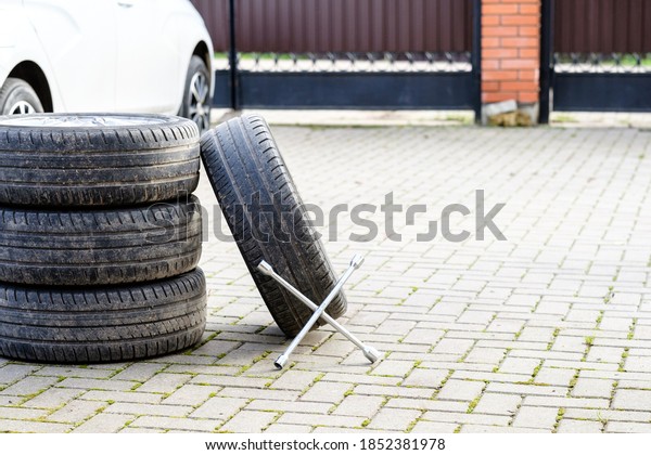 The wrench rests\
on the foot of the car wheels. An unknown white car on a blurred\
background. The concept of seasonal replacement of summer car tires\
with winter tires. Autumn\
day.