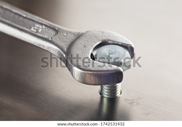 Wrench tightens  bolt in steel billet. Spanner,\
bolt, screw and nuts.