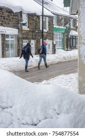 WREXHAM, UK - MARCH 22, 2013: Two People Walk Through A Wrexham Village While It Is Snowing. Walking In Road As Pavements Are Too Deep In Snow.