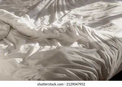 Wrinkle On Bedspread In The Morning Bedroom With Sunlight, Messy Bed After Night Sleep Concept, Rumpled Bed Sheet And Duvet Textile, Fabric And Linen Background.