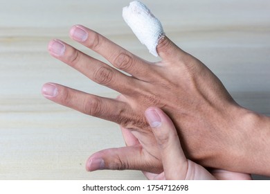 The Wrinkled Hand With The Little Finger Has To Be Treated As A Wound With A White Bandage. On A Wooden Table With Clipping Path