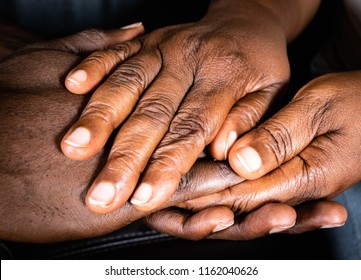 Wrinkled Hands of an elderly black woman holding the hand of a young African American man.  Old and young holding hands on dark background, closeup for retirement, support and Care concept
