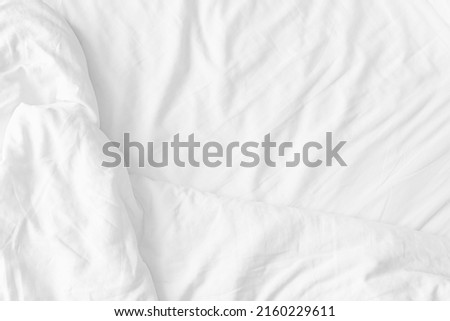 Wrinkled white bedsheet background. Top view of cozy fabric texture. Untidy duvet backdrop. Relaxation and comfortable accommodation.