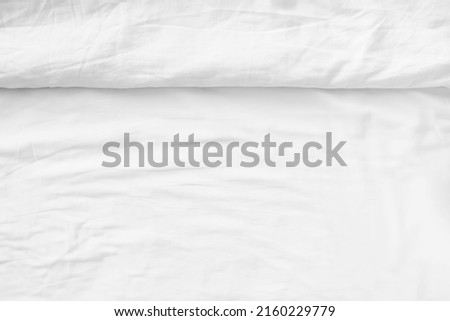 Wrinkled white bedsheet background. Top view of cozy fabric texture. Untidy duvet backdrop. Relaxation and comfortable accommodation.