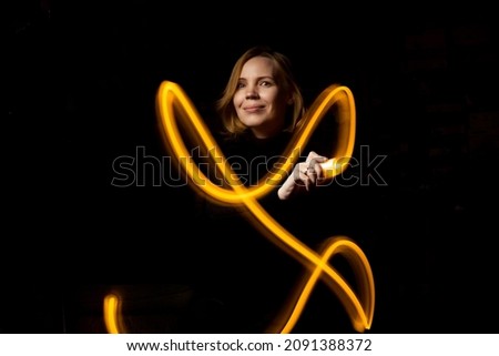 Write with light at long exposure in the dark. A middle-aged woman paints with a flashlight.