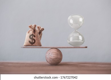 Write sand clock or hourglass and dollar bagson a balance scale in equal position on wood table. Financial concept : Time value of money, asset growth over time, depicts investment in long-term equity