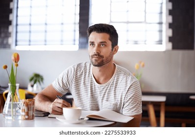 The write stuff. a handsome young man writing in a notebook while sitting at a restaurant table.