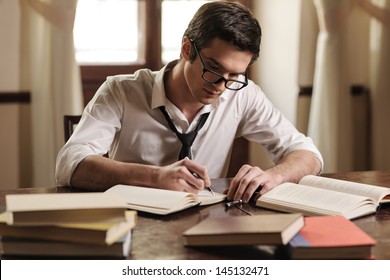 Writer at work. Handsome young writer sitting at the table and writing something in his sketchpad