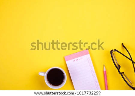 Writer's table flat lay composition. Student desk w/ supplies, blank notebook pages, black coffee cup, clipboard, pencil, planner, to do list, empty checkbox, glasses,. Copy space, yellow background