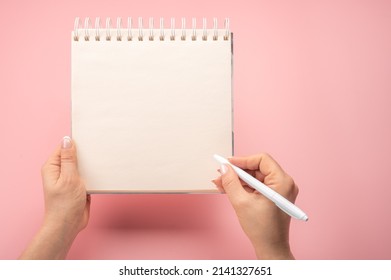 writing in blank notepad on pink background. female hands writing in mockup notepad. Woman writing in notepad. Mockup notepad with woman hands on pink table background
