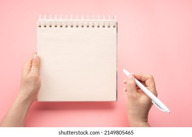 writing in blank notepad on pink background. Mockup notepad. woman hand with pen next to an empty blank notepad. top view of hand holding pen against spiral notepad on pink table, taking notes concept - Shutterstock ID 2149805465