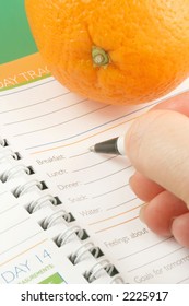 Writing In A Diet And Nutrition Journal With Orange To The Side