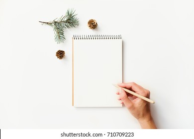 Writing Female Hand, Paper Notebook, Cones And Fir Branch On White Table. Top View.