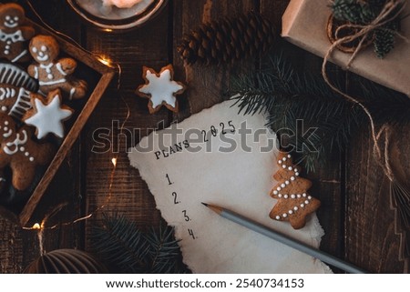 Writing new year resolutions 2025 by hand in December on New Year's Eve. Plan, goals, ideas, projects. Cozy home holiday atmosphere, Christmas lights, festive decor, homemade gingerbread cookies