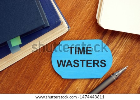 Writing note showing time wasters. The text is written on a small wooden board. Books, pen, notebook, wooden background are on the photo.