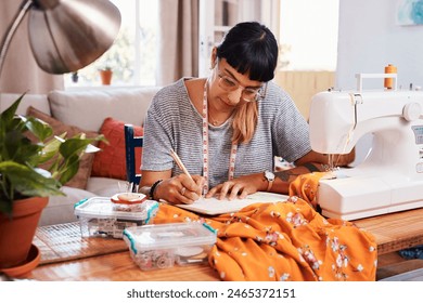 Writing, notes and female fashion designer in home studio for style with measuring tape for profession. Tailoring, sewing machine and cutting table with fabric for handmade clothing for business. - Powered by Shutterstock