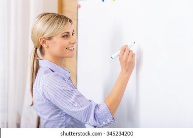 Writing On Whiteboard. Attractive Female Teacher Is Busy Writing On The Whiteboard During The Lesson. 