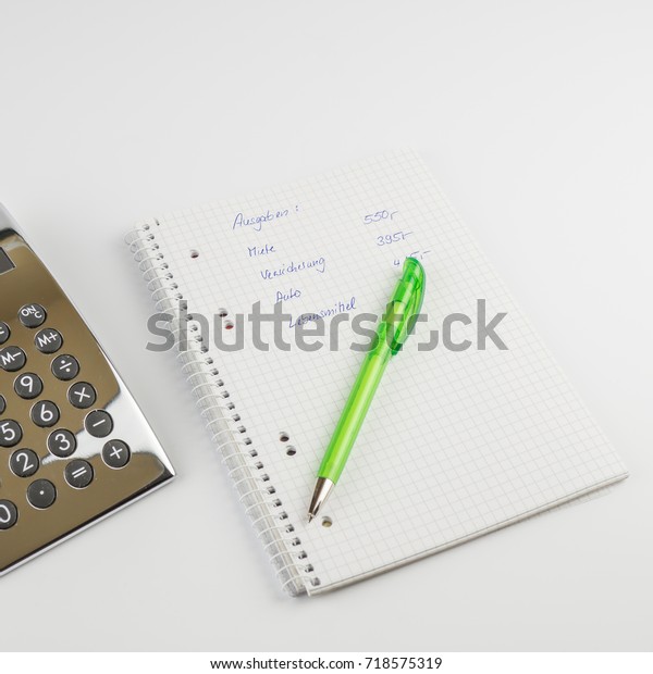 A writing pad with the German words for\
expenses, rent, insurance, car, lying on it, a ballpoint pen, next\
to it a calculator