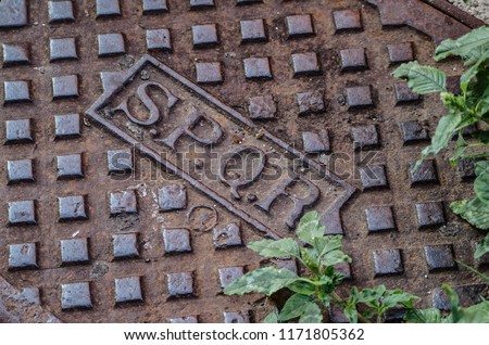 Written SPQR on a cast iron manhole with uncultivated grass under the sun of Rome