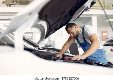 Wrker In A Car Salon. Expert Checks The Car. Man In A Blue Uniform.