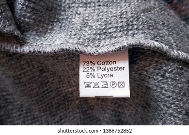 Wrong Side Of A Gray Dress Made Of Wool, The Composition Is Specified: Cotton, Polyester And Lycra. Fabric Composition Clothes Label On Gray Texture Background.