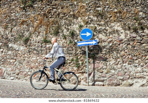 Wrong way. Businessman going on bicycle the\
wrong direction
