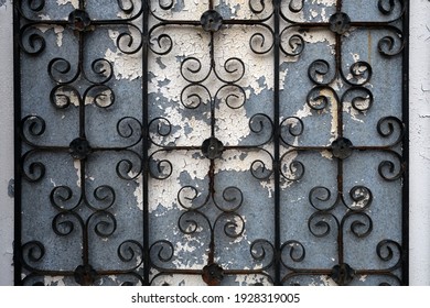 Wrought iron fence or gate on a weathered blue wall with cracked white paint.