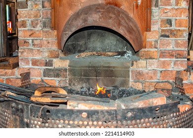 A Wrought Iron Furnace In An Old Brick Blacksmith Forge With A Coal Burning Flame And Fire Inside An Old Forge. The Industrial Forging Workshop Has A Number Of Tongs, Hammers, And Vintage Tools.  