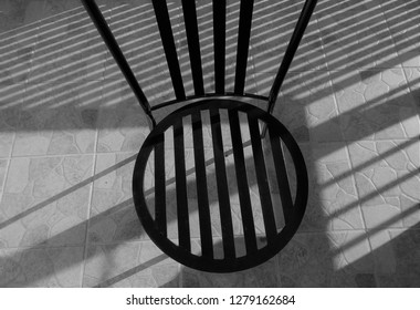 Wrought Iron Garden Chair Creating Shadows Upon Shadows On Patio Tiles.