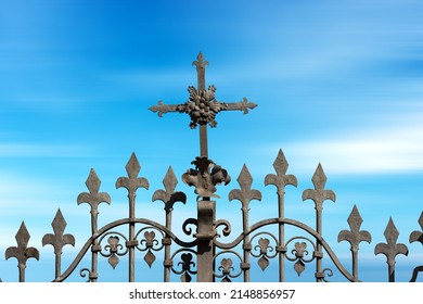 Wrought iron gate with a Religious Cross and sharp points against a blurred blue sky with clouds and copy space. Brescia, Lombardy, Italy, Europe.