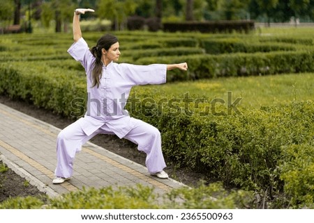 Wushu master in kimono uniform training on the park lawn. Kungfu champion trains maritial arts in nature on background of trees 