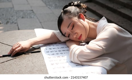 Wuxi, China - March 2022: An Asian beauty in Chinese vintage dress sleeping on a piece of cloth written with a Chinese ancient poem named Chi Bi Huai Gu by Su Shi, a poet of Song Dynasty. 