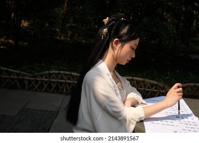 Wuxi China - March 2022: An Asian lady dressed up in vintage style writing an ancient poem named Chi Bi Huai Gu composed by Shi Su, an ancient poet, in a sunny spring day. Chinese brush pen. 