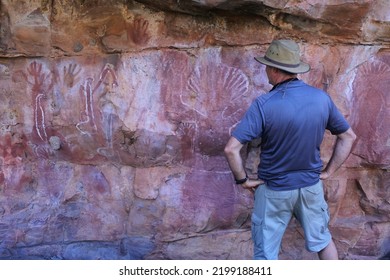 WYNDHAM, WA - AUG 12 2022:Australian Man Looking At Australian Aboriginal Mythology Rock Paintings On A Rock Cave In Kimberley Western Australia.