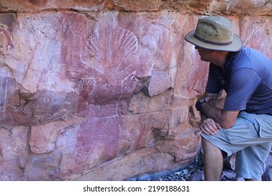 WYNDHAM, WA - AUG 12 2022:Australian Man Looking At Australian Aboriginal Mythology Rock Paintings On A Rock Cave In Kimberley Western Australia.