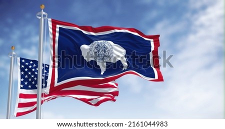 The Wyoming state flag waving along with the national flag of the United States of America. Wyoming is a state in the Mountain West subregion of the Western United States