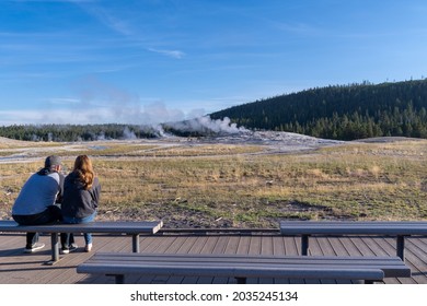 Wyoming, USA - August 11, 2021: Young Couple Waits On The Benches For Old Faithful To Erupt In The Morning