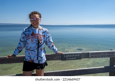 Wyoming, USA - July 19, 2022: Goofy Tourist Woman Wearing A Tacky Souviner Sweatshirt Poses At Lakeshore Geyser In Yellowstone National Park