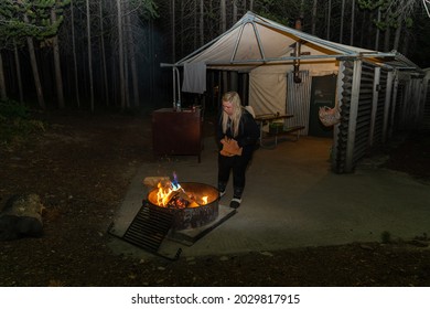 Wyoming, USA - June 26, 2021: Blonde Woman Wearing Pajamas Starts A Fire In A Designated Fire Ring Outside Of A Tent Cabin In Colter Bay Grand Teton National Park