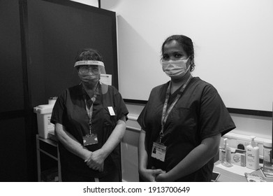 Wythenshawe, Manchester, UK February 2021:Black and white photo of two nurses under stress in a covid vaccination clinic wearing face shield and surgical masks