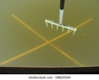 X Marks The Spot For The Sturgeon Spear.  Spear Is Positioned Above A Hole In An Ice Shack Or Shanty With A Yellow X Marked On Bottom Of Lake To Help See Through Cloudy Water.  Waiting For Sturgeon.