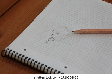 X plus Y equals ? (x+y=?) written on checkered notebook and the pencil on the notebook. 