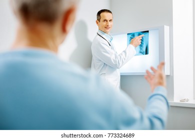 X ray diagnostics. Nice delighted male therapist pointing at the X ray photo and looking at his patient while putting a diagnosis