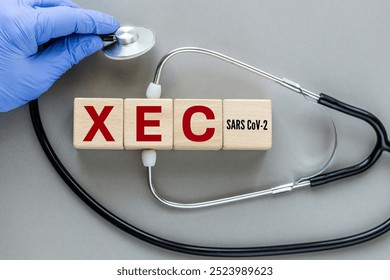 XEC, the latest subvariant of the SARS CoV-2 virus. The name of the Xec virus causing Covid-19 disease on wooden cubes. Stethoscope in doctor's hand, Medical concept, gray background, flat lay