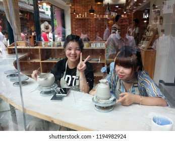 Xiamen, China - October 2018: Smiling Chinese Girls Make Clay Pots In The Workshop On The Island Of Gulangyu, View Through The Window. Pottery Making Concept, Tourism In China