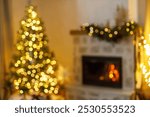 Xmas background. Blurred image of stylish christmas tree with golden lights bokeh and burning fireplace in evening living room. Defocused atmospheric christmas eve at home.